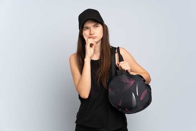 Young sport girl with sport bag isolated on grey having doubts and thinking