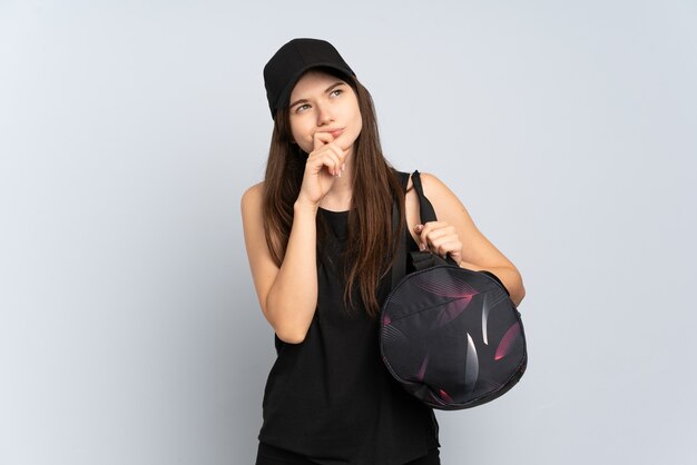 Young sport girl with sport bag isolated on grey and looking up