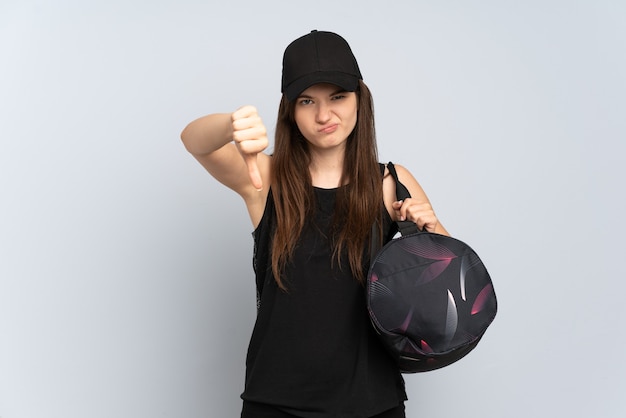 Young sport girl with sport bag isolated on grey showing thumb down