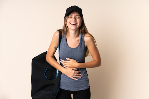 Young sport Lithuanian woman holding a sport bag isolated on beige background smiling a lot