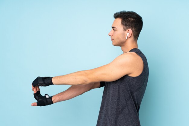 Young sport man over on blue wall stretching arm