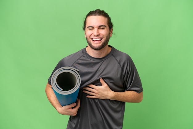 Young sport man going to yoga classes while holding a mat over isolated background smiling a lot
