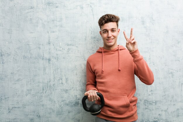 Young sport man holding a dumbbell showing number two with fingers.