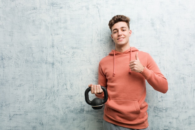 Young sport man holding a dumbbell smiling and raising thumb up