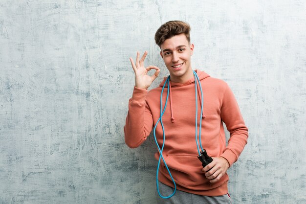 Young sport man holding a jump rope cheerful and confident showing ok gesture.
