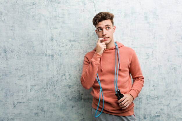 Young sport man holding a jump rope relaxed thinking about something looking at a copy space.