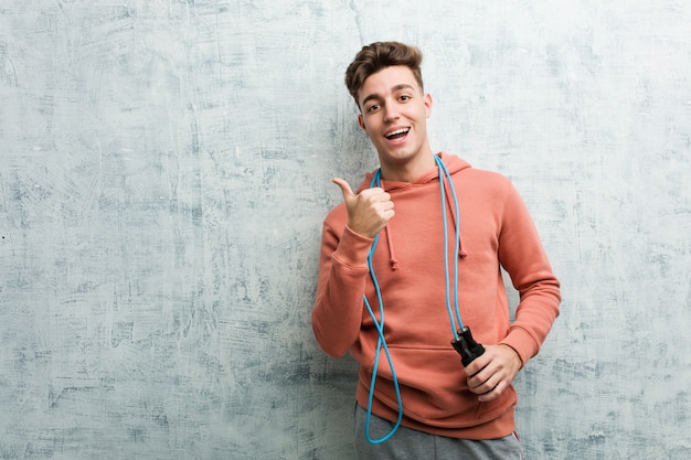 Young sport man holding a jump rope smiling cheerfully pointing with forefinger away