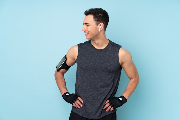 Young sport man over isolated on blue wall posing with arms at hip and looking side