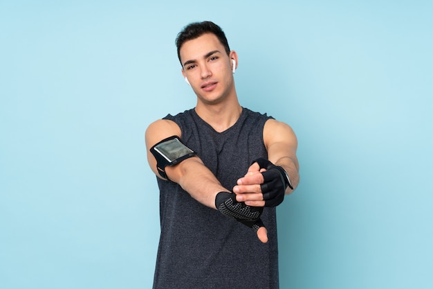 Young sport man over isolated on blue wall stretching arm