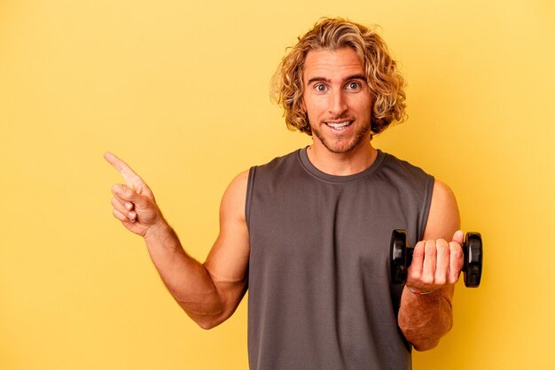 Young sport man making weightlifting isolated on yellow background smiling and pointing aside, showing something at blank space.