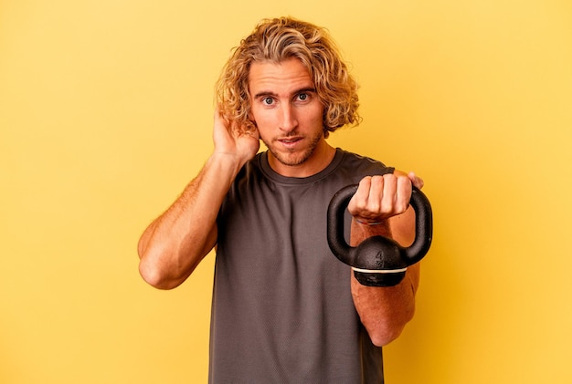 Young sport man making weightlifting isolated on yellow background trying to listening a gossip.