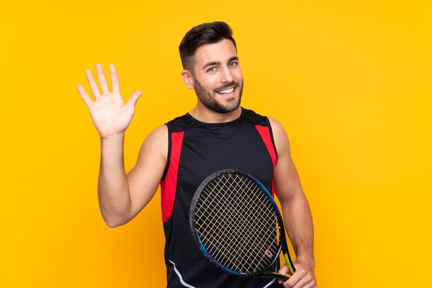 Young sport man playing tennis over isolated wall