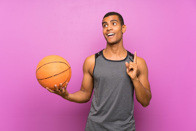 Young sport man with ball of basketball over isolated purple wall intending to realizes the solution while lifting a finger up