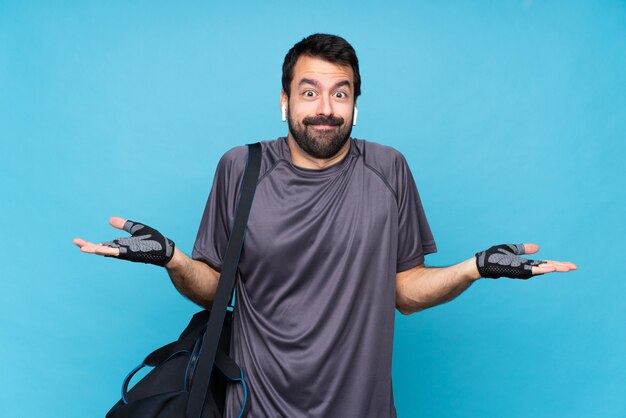 Young sport man with beard over isolated blue  having doubts while raising hands