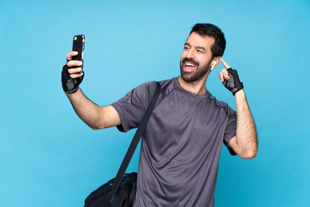 Giovane uomo di sport con la barba sopra il blu isolato che fa un selfie