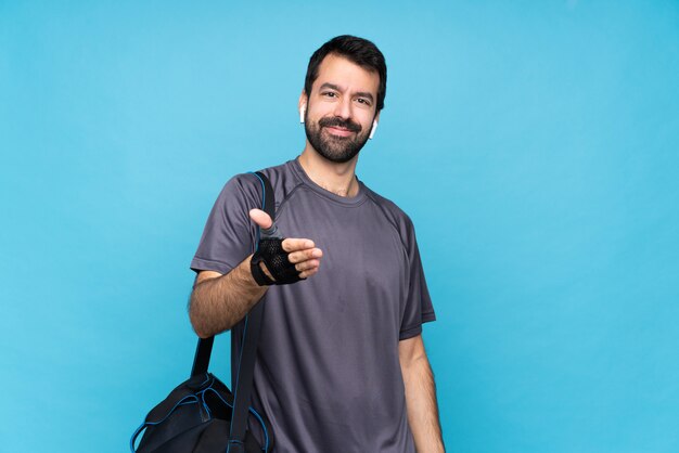 Young sport man with beard over isolated blue shaking hands for closing a good deal