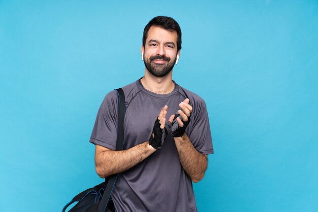 Young sport man with beard over isolated blue wall applauding after presentation in a conference