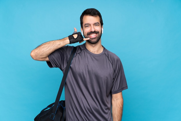 Young sport man with beard over isolated blue wall making phone gesture. Call me back sign