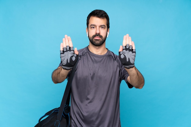 Young sport man with beard over isolated blue wall making stop gesture and disappointed