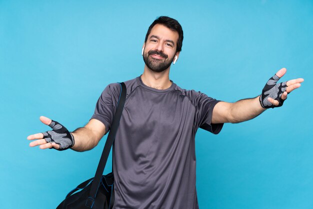 Young sport man with beard over isolated blue wall presenting and inviting to come with hand