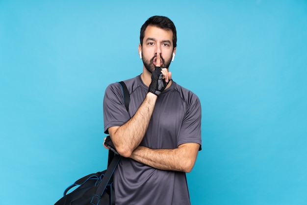 Young sport man with beard over isolated blue wall showing a sign of silence gesture putting finger in mouth