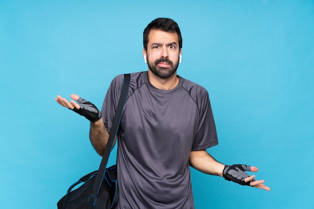 Giovane uomo di sport con la barba sopra la parete blu isolata infelice per non capire qualcosa