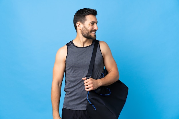 Young sport man with sport bag isolated on blue background looking side