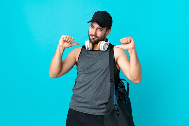 Foto giovane uomo sportivo con borsa sportiva isolato su sfondo blu orgoglioso e soddisfatto di sé