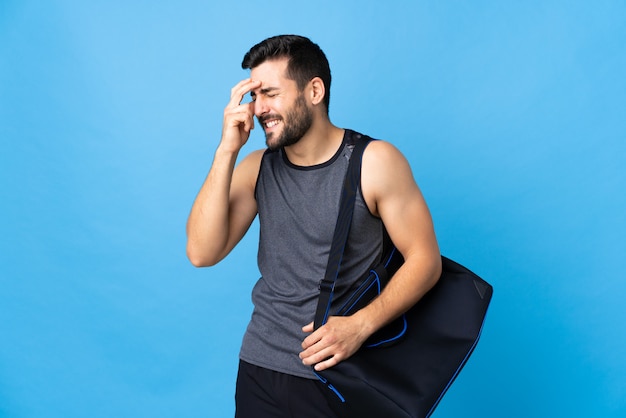 Young sport man with sport bag isolated on blue wall laughing