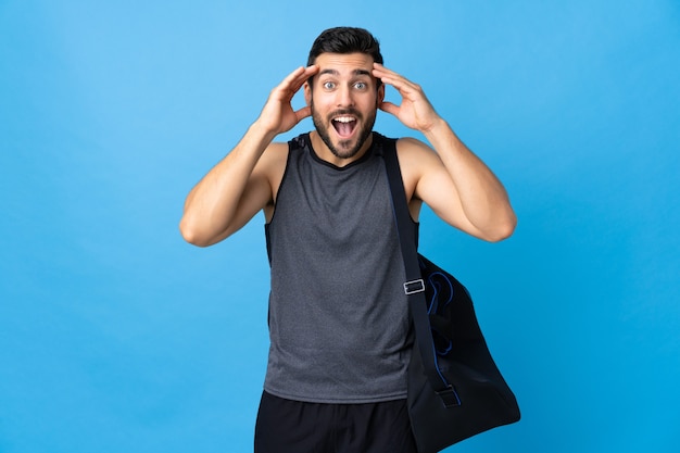 Young sport man with sport bag isolated on blue with surprise expression