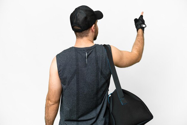 Young sport man with sport bag over isolated white background pointing back with the index finger