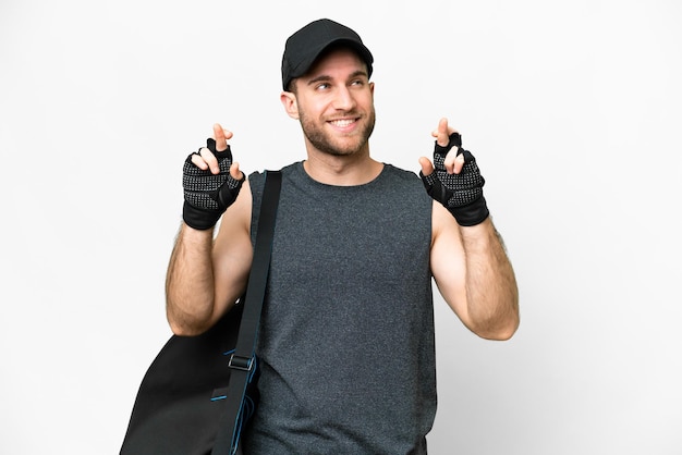 Young sport man with sport bag over isolated white background with fingers crossing