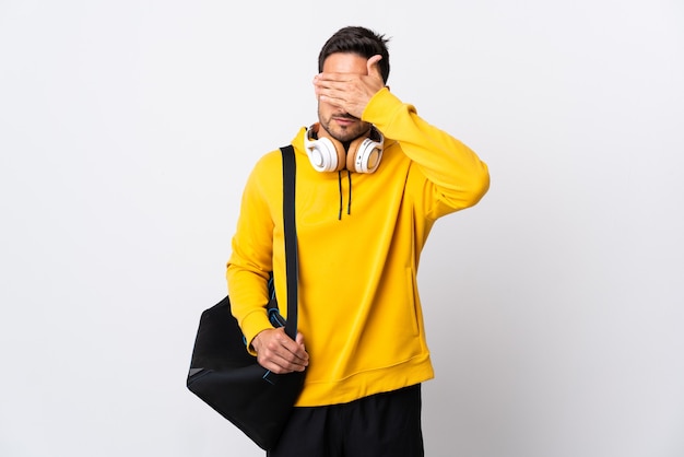 Young sport man with sport bag isolated on white covering eyes by hands. Do not want to see something