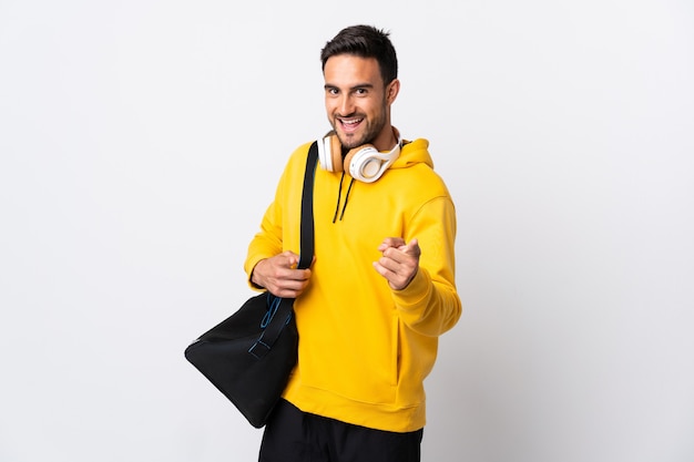 Giovane uomo di sport con borsa sportiva isolata su bianco che punta verso la parte anteriore e sorridente