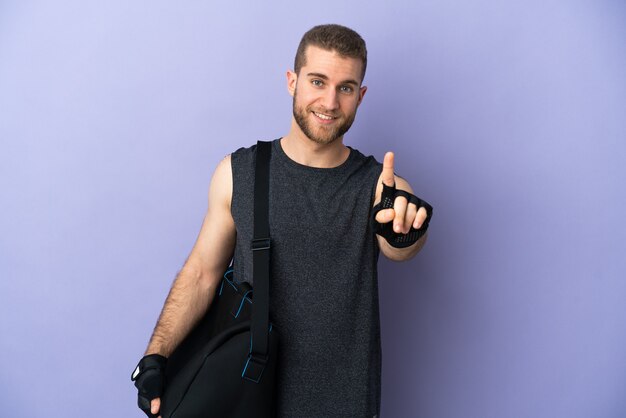 Young sport man with sport bag isolated on white showing and lifting a finger