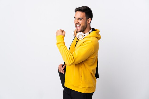 Young sport man with sport bag isolated on white wall celebrating a victory