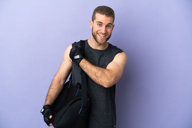 Young sport man with sport bag isolated on white wall celebrating a victory