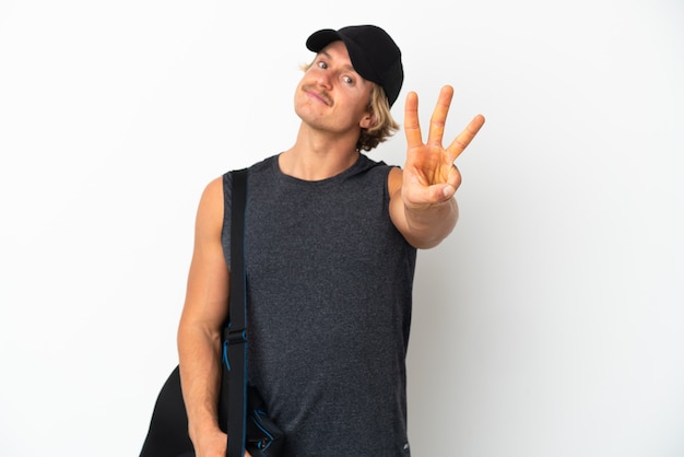 Young sport man with sport bag isolated on white wall happy and counting three with fingers