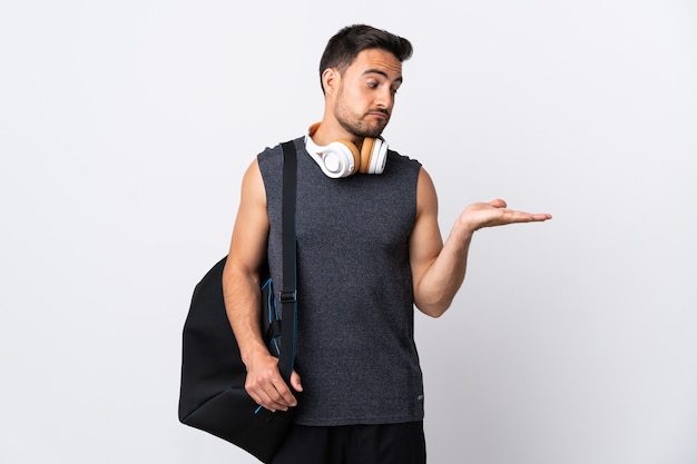 Young sport man with sport bag isolated on white wall holding copyspace with doubts