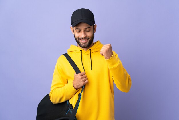 Young sport Moroccan man with sport bag isolated on purple celebrating a victory