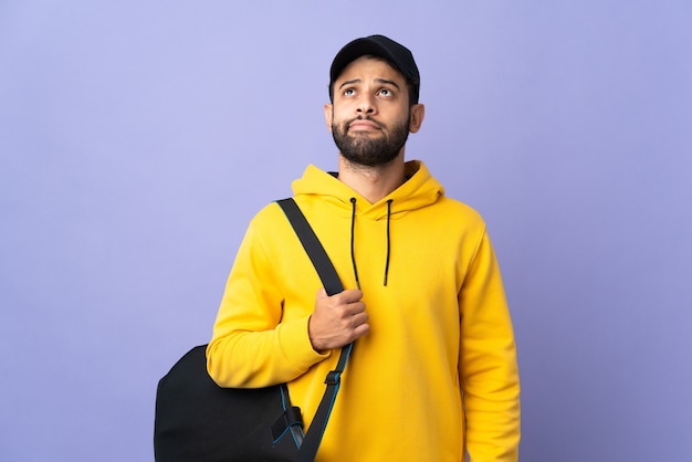 Young sport Moroccan man with sport bag isolated on purple and looking up