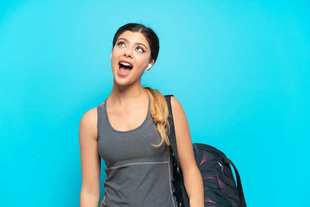 Young sport Russian girl with sport bag isolated on blue background laughing