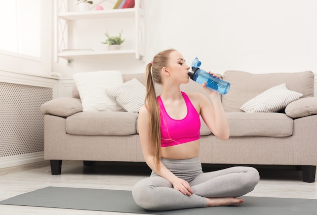 Acqua potabile della giovane donna di sport a casa. ragazza sicura di forma fisica che tiene la bottiglia, riposa dopo l'allenamento, concetto di stile di vita sano, copia spazio