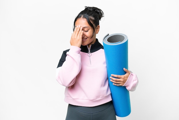 Young sport woman going to yoga classes while holding a mat over isolated white background laughing