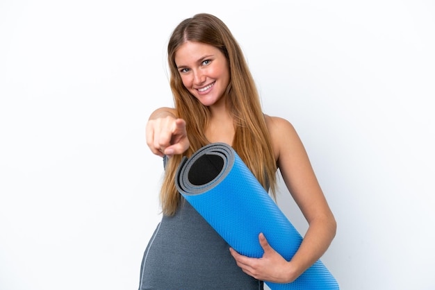 Young sport woman going to yoga classes while holding a mat pointing front with happy expression