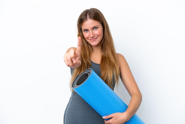 Giovane donna sportiva che va alle lezioni di yoga mentre tiene in mano un tappetino che mostra e solleva un dito