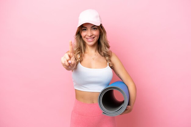 Photo young sport woman going to yoga classes while holding a mat showing and lifting a finger