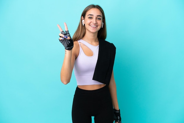 Young sport woman isolated on blue background smiling and showing victory sign