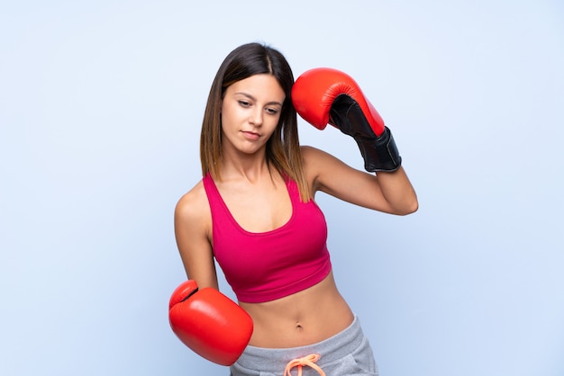 Young sport woman over isolated blue with boxing gloves