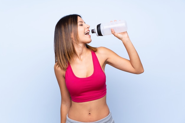 Young sport woman over isolated blue with sports water bottle